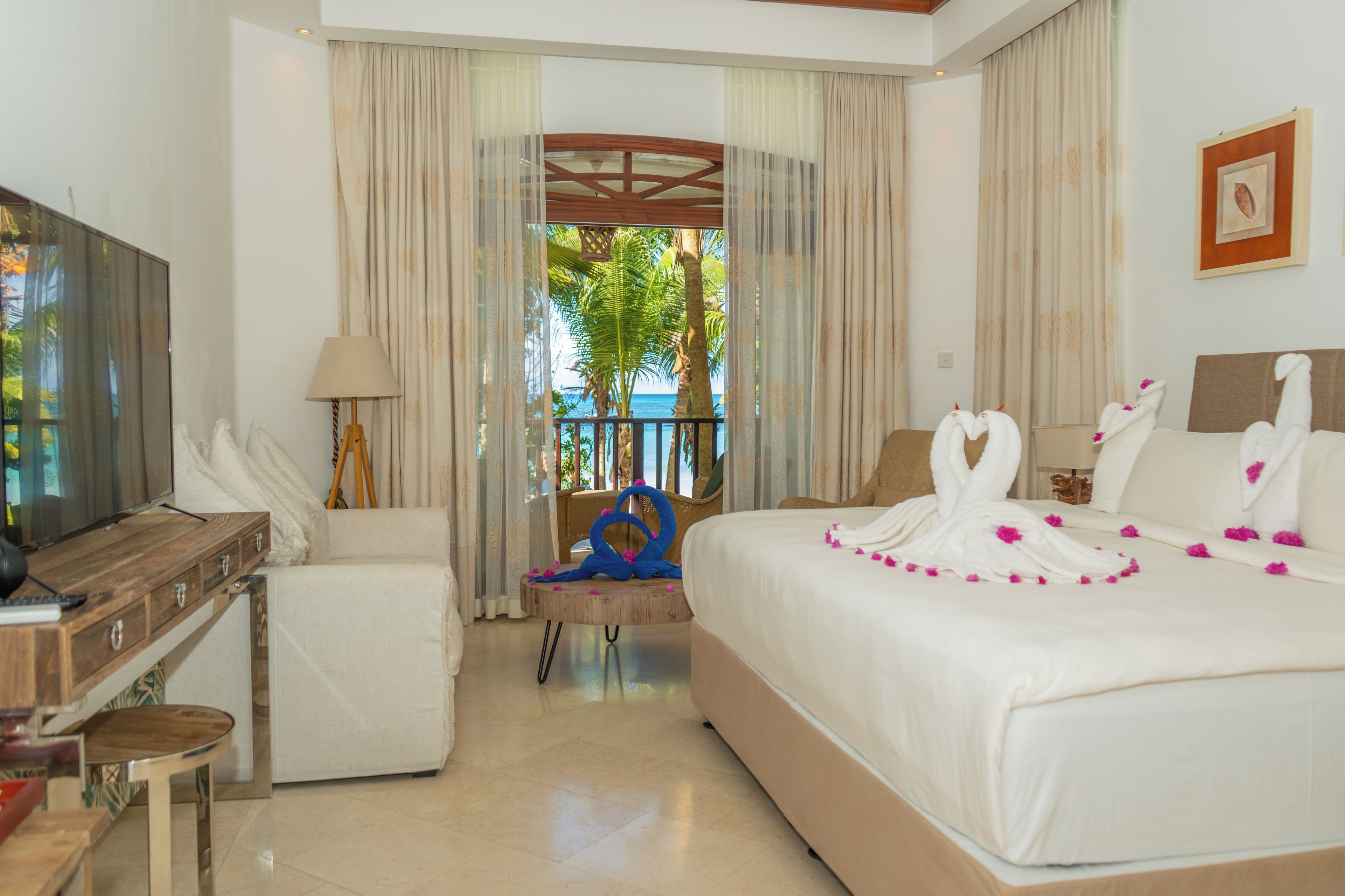 A hotel room with a bed, a desk, a chair, a TV, and a view of the sea.