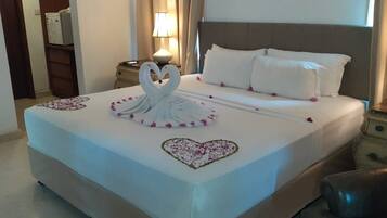 Una habitación de hotel con una cama bien hecha, una decoración con forma de corazón sobre la cama y una mesita de noche con lámpara.