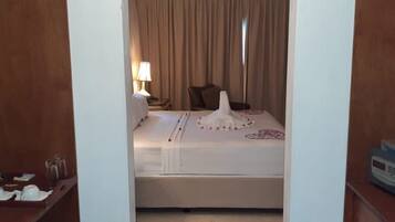 A hotel room with a bed, a nightstand with a lamp, a chair, and a bedside table with a remote control.