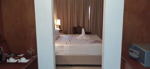 A hotel room with a bed, a nightstand with a lamp, a chair, and a bedside table with a remote control. - Village du Pecheur (Praslin Island)