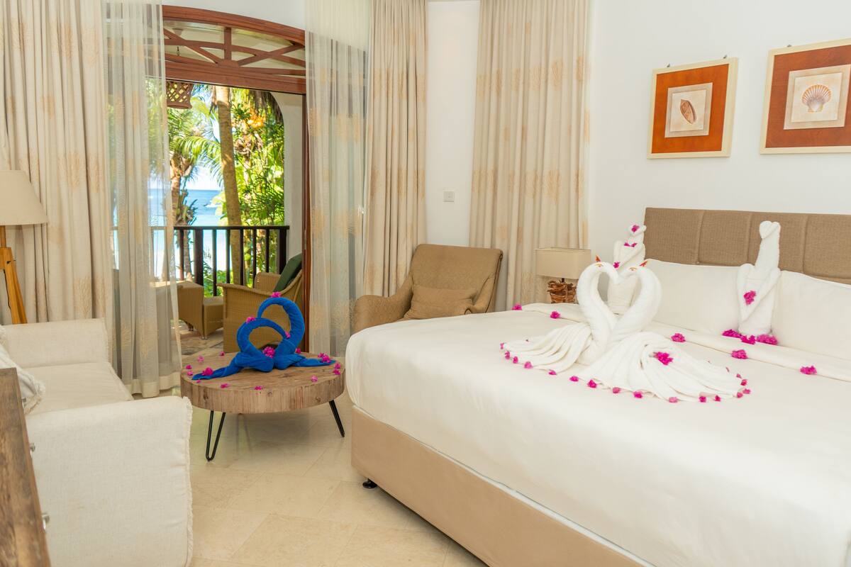 A hotel room with a bed, a chair, a small table, and a view of the outdoors.