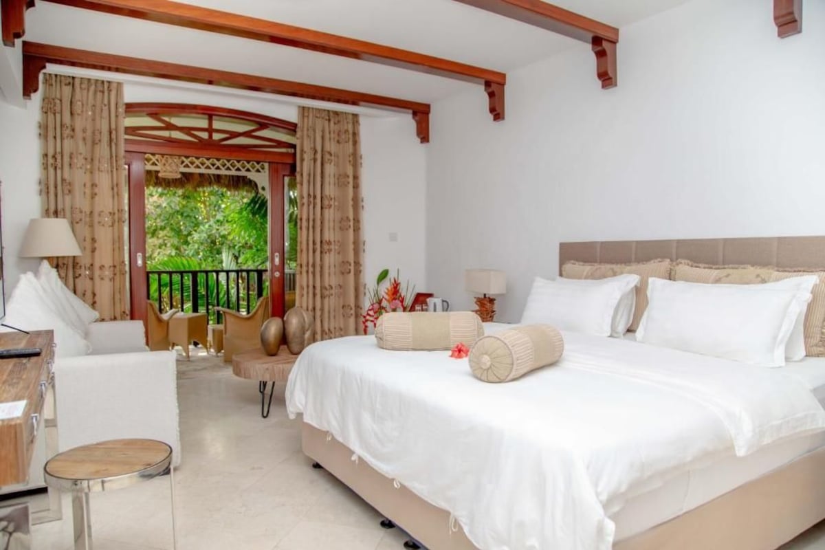 A bedroom with a bed, a desk, and a chair. There is a balcony with curtains.