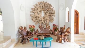 Un vestíbulo con una gran escultura de madera, un banco y dos jarrones con flores.