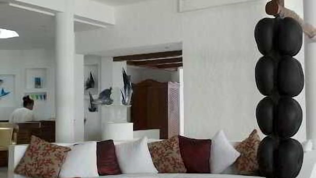 A modern living room with a white sofa set, red and black accent pillows, and a unique black column sculpture. - Village du Pecheur (Praslin Island)