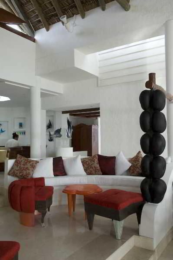 Un salon moderne avec un canapé blanc, des coussins décoratifs rouges et noirs, et une sculpture originale en forme de colonne noire.