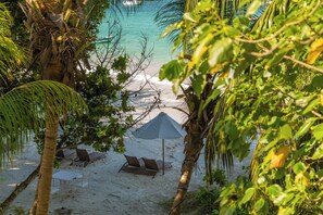 A beach with white sand, palm trees, and a few lounge chairs. - Village du Pecheur (Praslin Island)