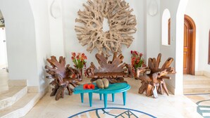 A lobby with a central seating area, a large abstract wall art piece, and a wooden sculpture. - Village du Pecheur (Praslin Island)