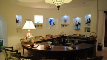 A bar area with a round table, chairs, and a lamp. There are framed pictures on the wall.
