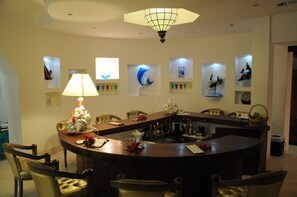 A bar area with a round table, chairs, and a lamp. There are framed pictures on the wall. - Village du Pecheur (Praslin Island)