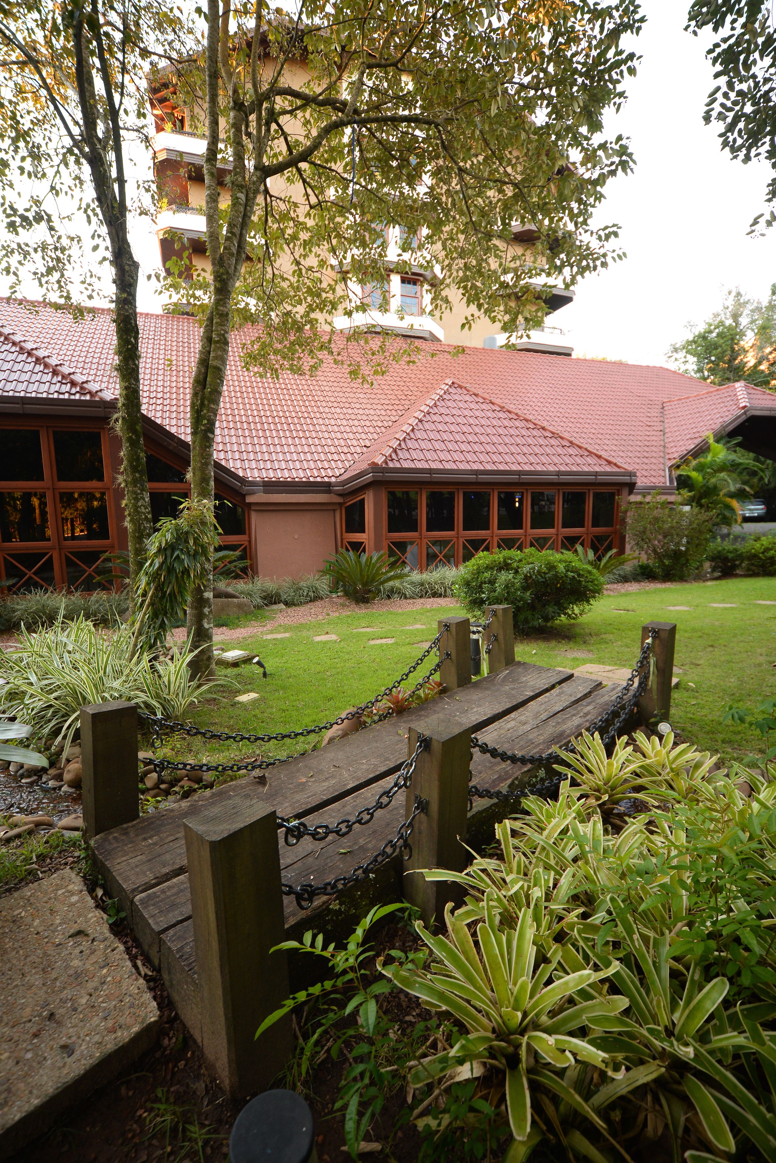 Un patio con un banco de madera, un edificio de techo rojo y diversas plantas.
