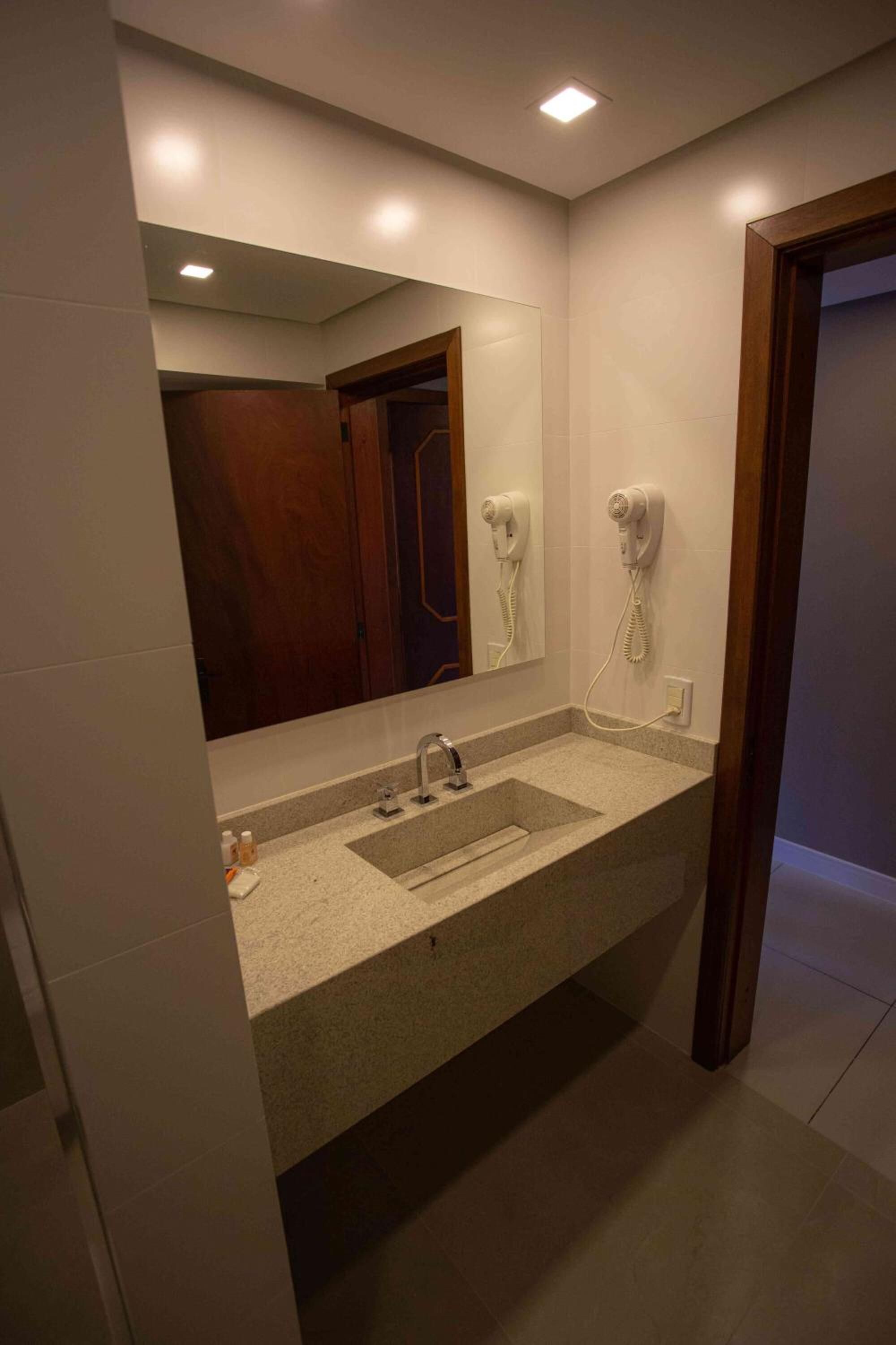 A modern bathroom with a large mirror, a sink, and two hair dryers mounted on the wall.