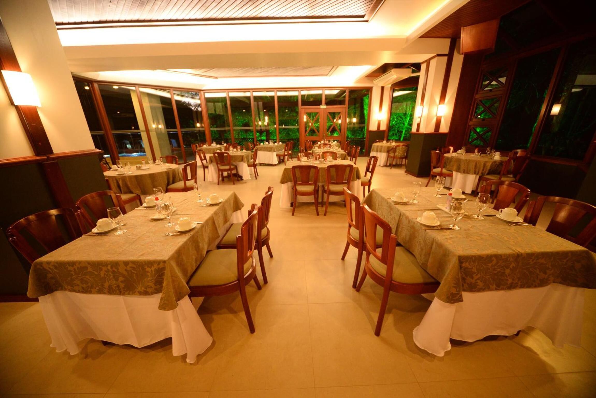 A restaurant with multiple tables set for dining, large windows, and a warm interior lighting.