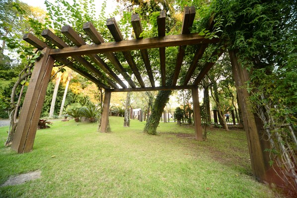 Una estructura de pérgola de madera en un jardín con césped y árboles.