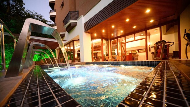 Een hoek met een hottub, een betegelde vloer, een metalen constructie en een gebouw met grote ramen en een houten plafond.