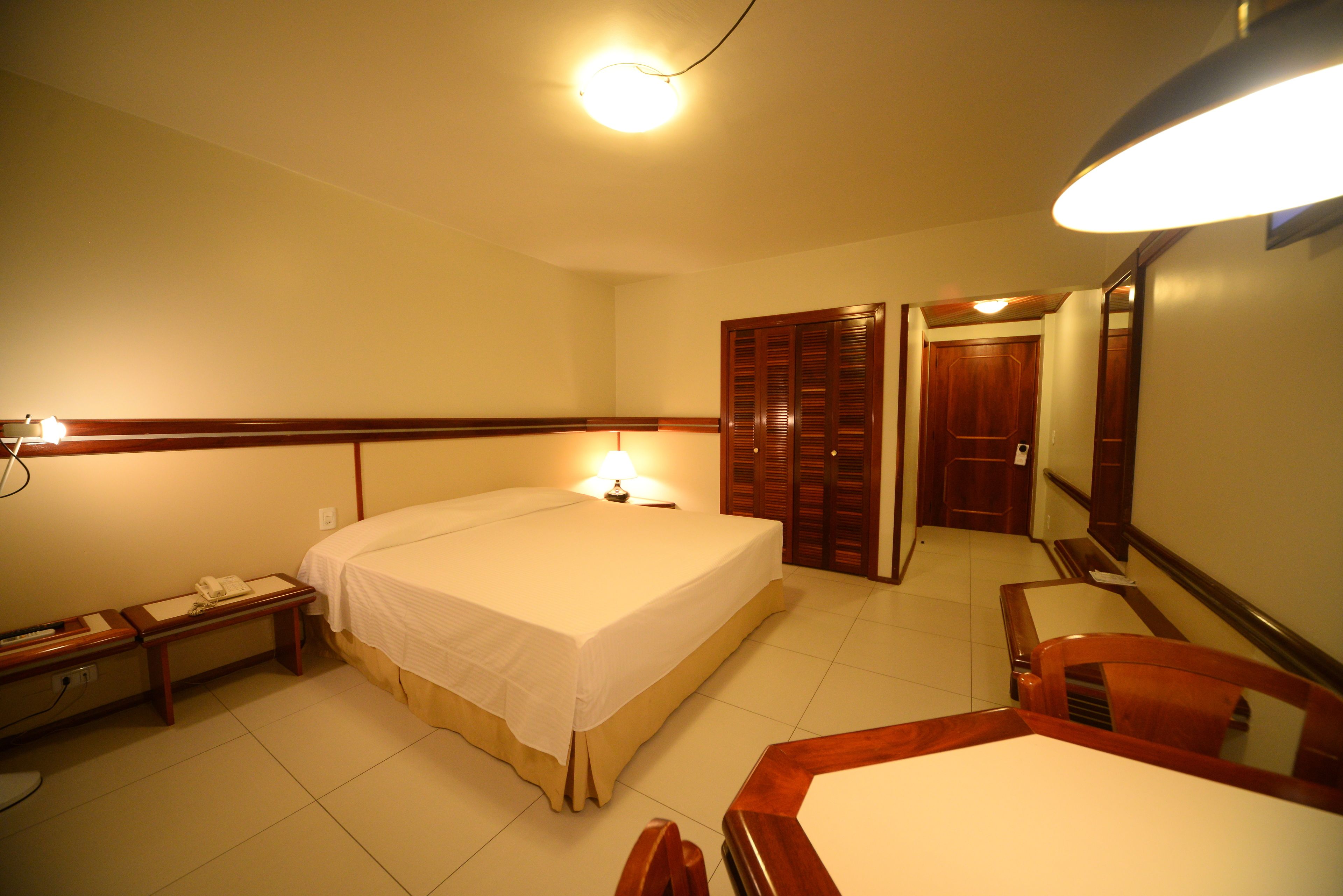 A hotel room with a bed, bedside table, lamp, and a mirror.