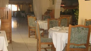 Zona de dinar d'hotel amb taules i cadires de fusta, un paviment de rajola i vista al passadís.