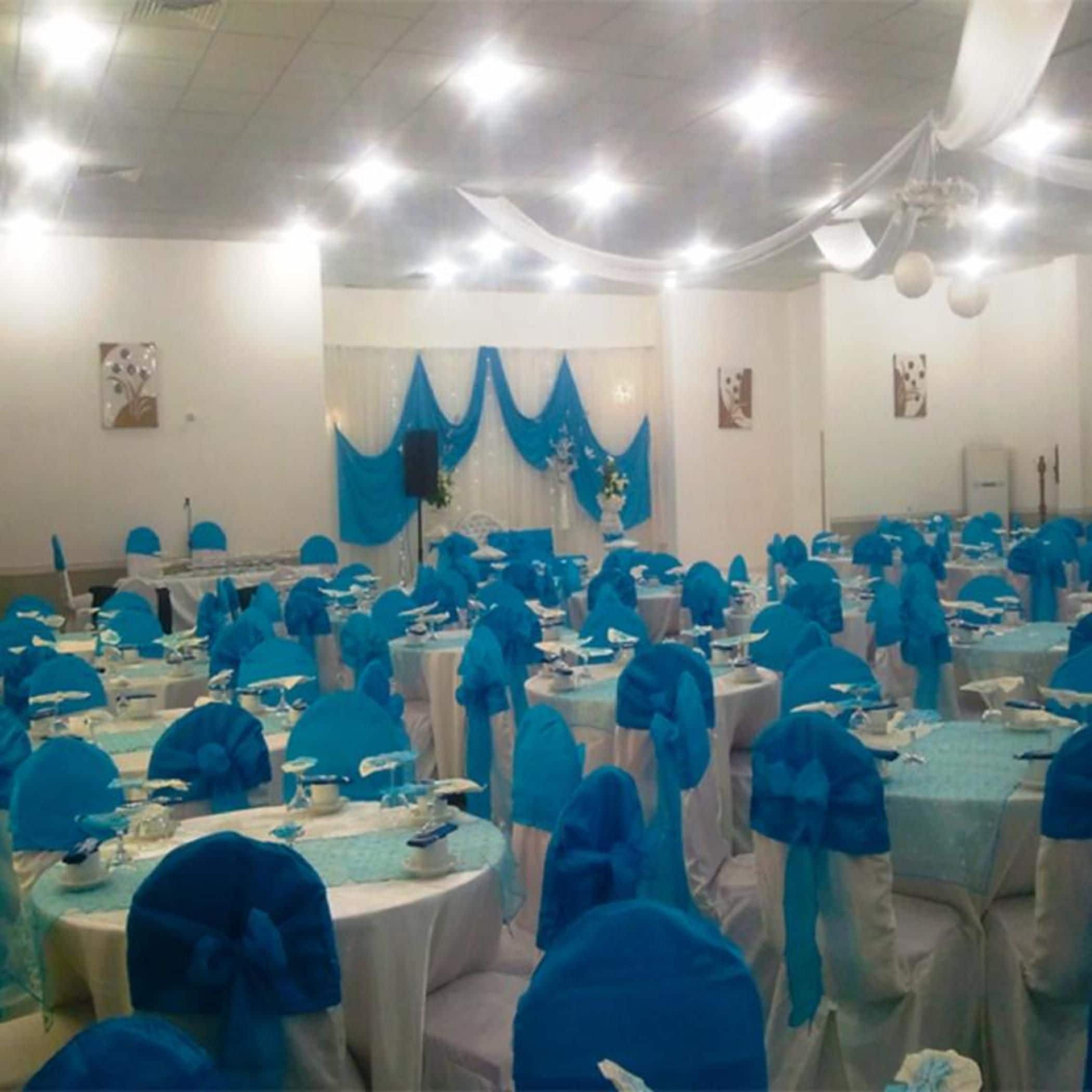 Un salón de banquetes con mesas redondas cubiertas con manteles blancos y fundas de asiento azules.