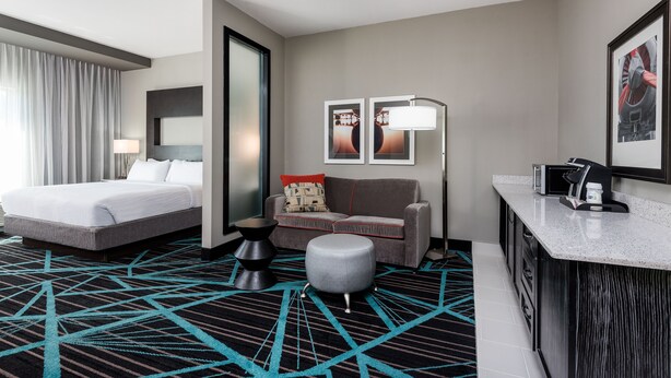 A hotel room with a bed, a sofa, a small table, a lamp, and a desk with a computer. - Holiday Inn Express & Suites Charlotte Airport by IHG (Charlotte)