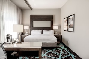 A hotel room with a large bed, bedside tables with lamps, a desk, a coffee machine, and a patterned carpet.