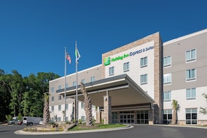 A Holiday Inn Express & Suites building with a covered entrance, multiple windows, and flags. - Holiday Inn Express & Suites Charlotte Airport by IHG (Charlotte)