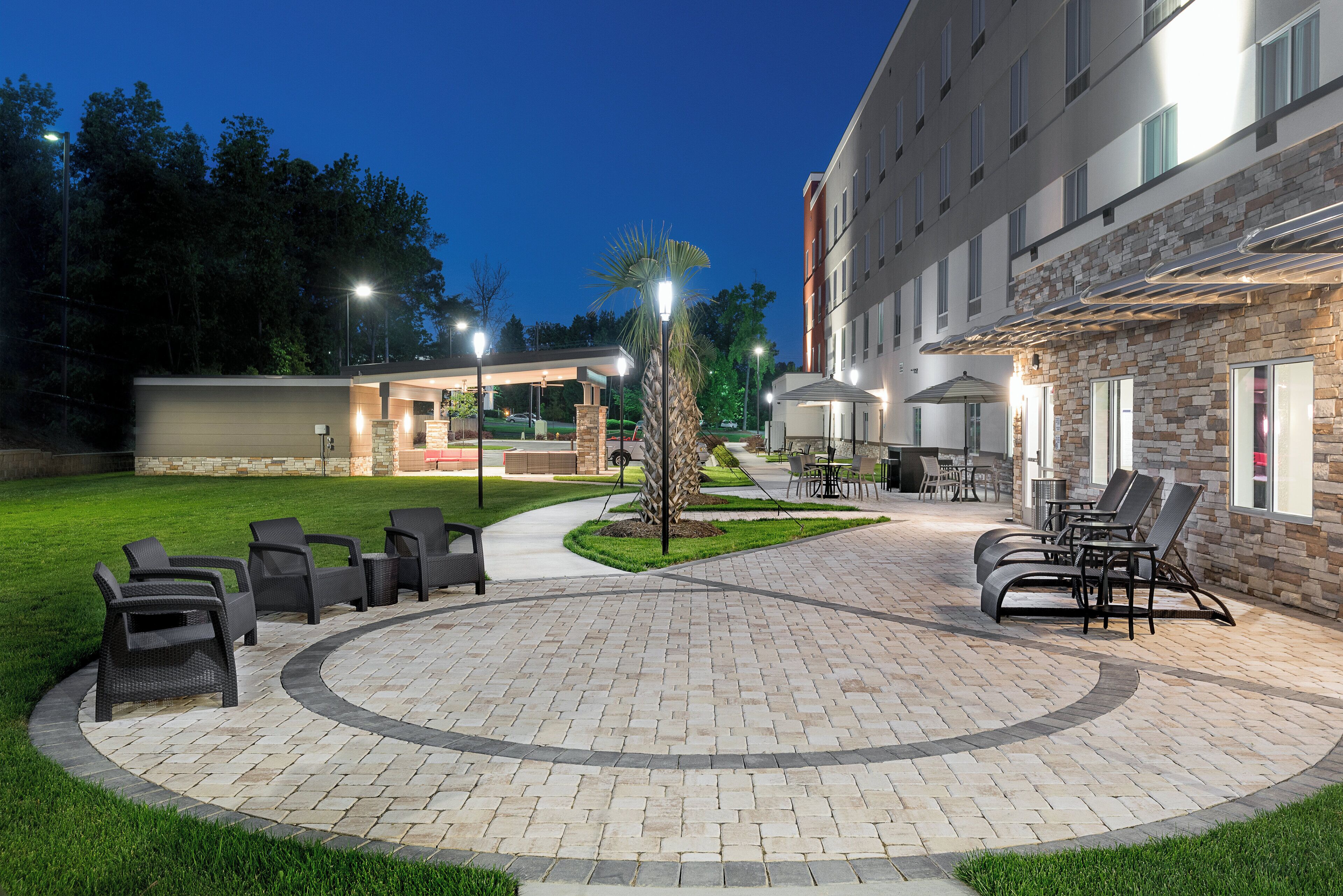 Un espace extérieur bien éclairé, aménagé avec des meubles de jardin et un chemin menant à l’entrée d’un bâtiment.