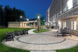 A well-lit outdoor patio area with seating arrangements and a pathway leading to a building entrance. - Holiday Inn Express & Suites Charlotte Airport by IHG (Charlotte)