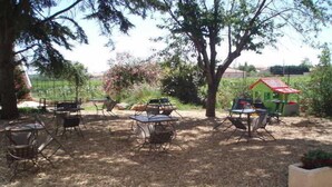 Eine Außenpatio-Terrasse mit Tischen und Stühlen, umgeben von Bäumen und einem Garten.