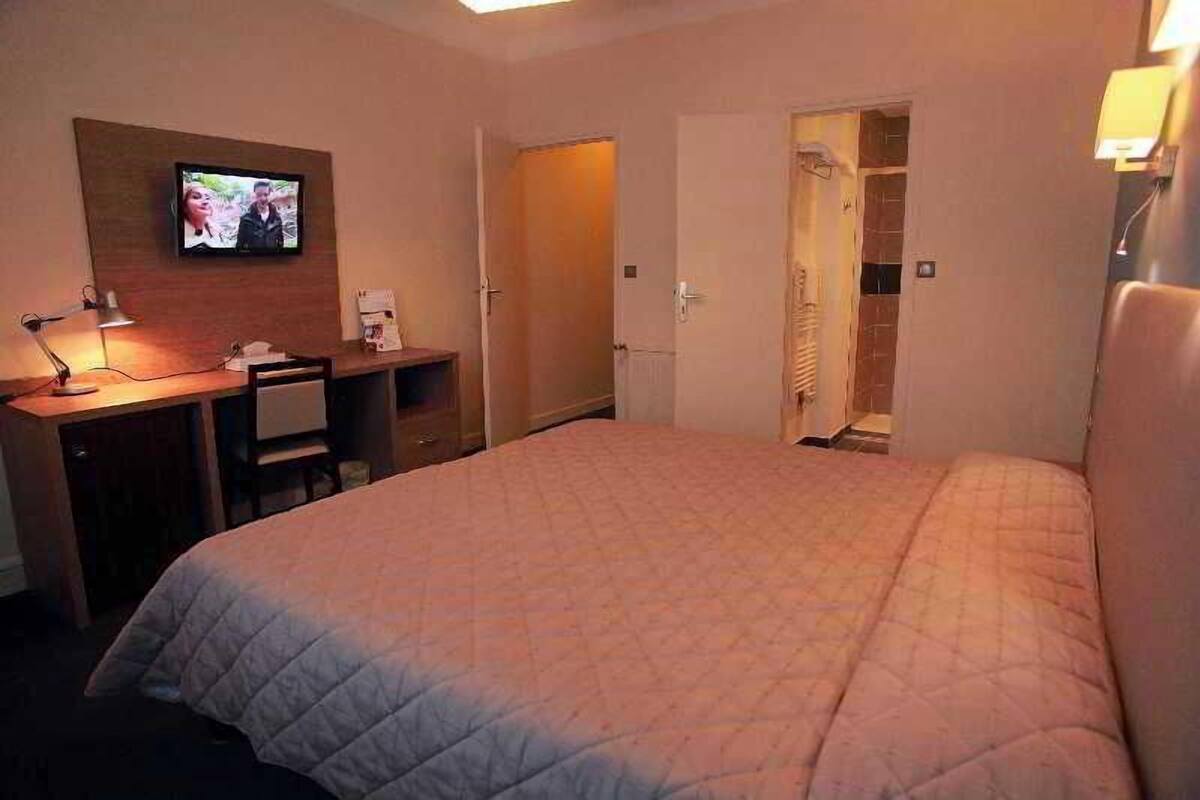 A hotel room with a bed, a desk with a lamp, a television, and a walk-in closet.