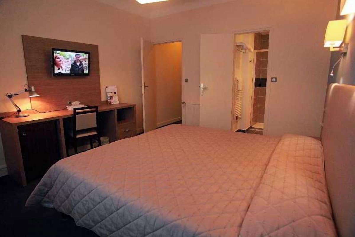 A hotel room with a bed, a desk with a lamp, a television, and a walk-in closet.