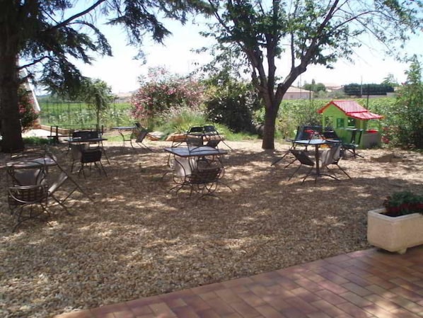 Un patio al aire libre con mesas y sillas, rodeado de árboles y un jardín.