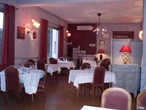 Comedor con mesas dispuestas para el servicio, sillas y un aparador con una lámpara.