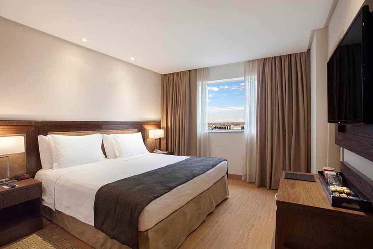 Habitación de hotel con una cama grande, televisión, escritorio con una bandeja de aperitivos y ventana con cortinas.