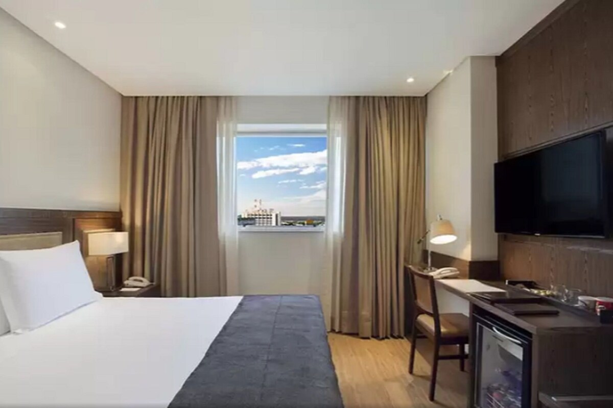 Ein Hotelzimmer mit Bett, Schreibtisch, Fernseher und einem Fenster mit Vorhängen.