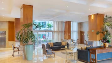 A spacious lobby with a modern design, featuring a large seating area with sofas and armchairs, a coffee table, and a reception desk.