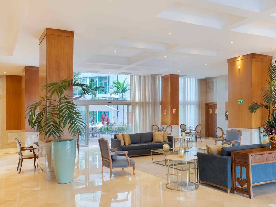 A spacious lobby with a modern design, featuring a large seating area with sofas and armchairs, a coffee table, and a reception desk.