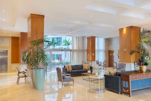 Um hall amplo com design moderno, com uma grande área de estar com sofás e poltronas, uma mesa de centro e um balcão de recepção.