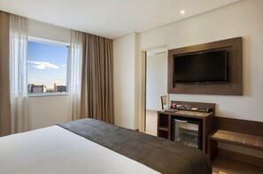 Une chambre d’hôtel avec un grand lit, un téléviseur fixé au mur, une petite kitchenette et une fenêtre avec des rideaux.