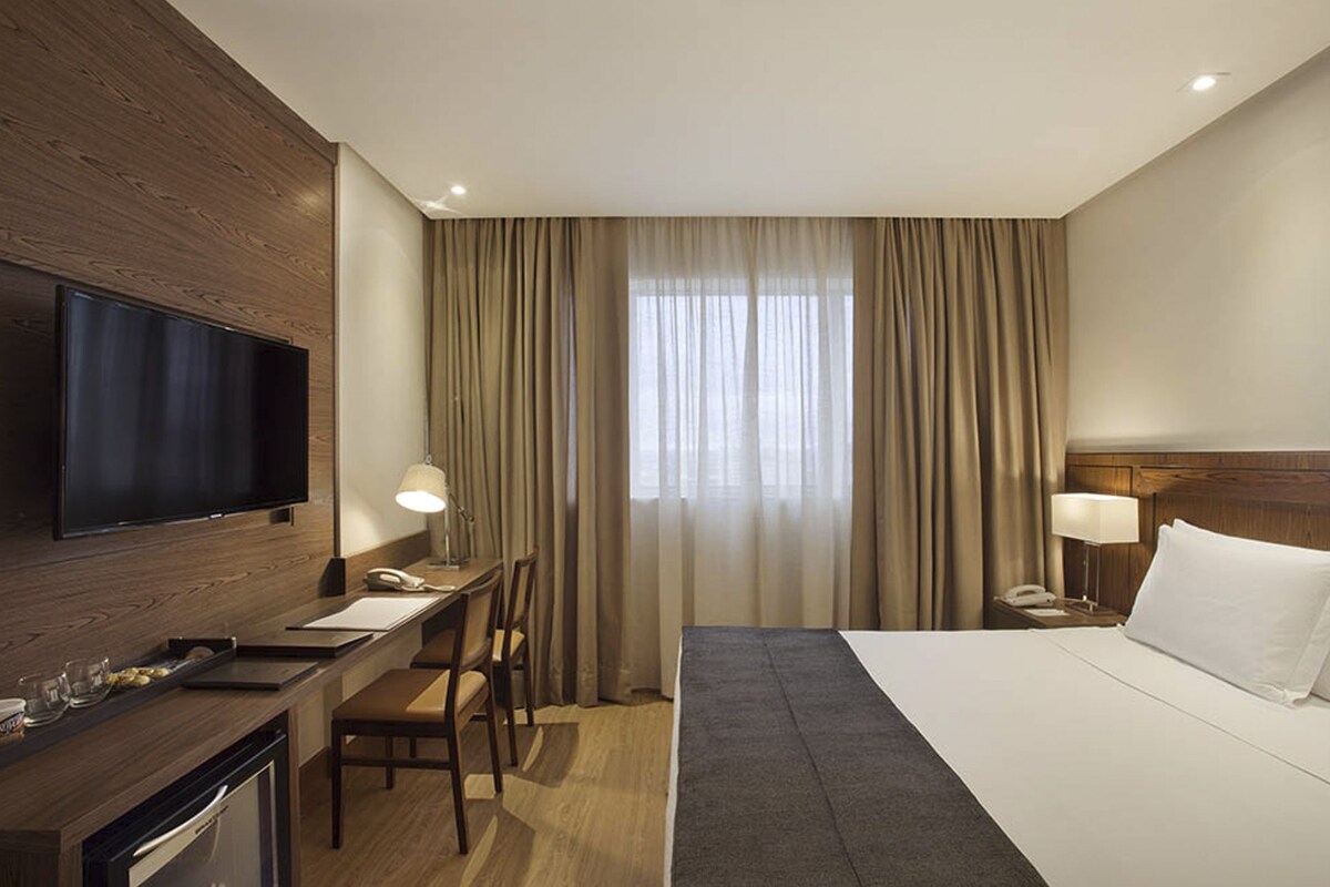 Ein Hotelzimmer mit Bett, Schreibtisch, Fernseher und einem Fenster mit Vorhängen.