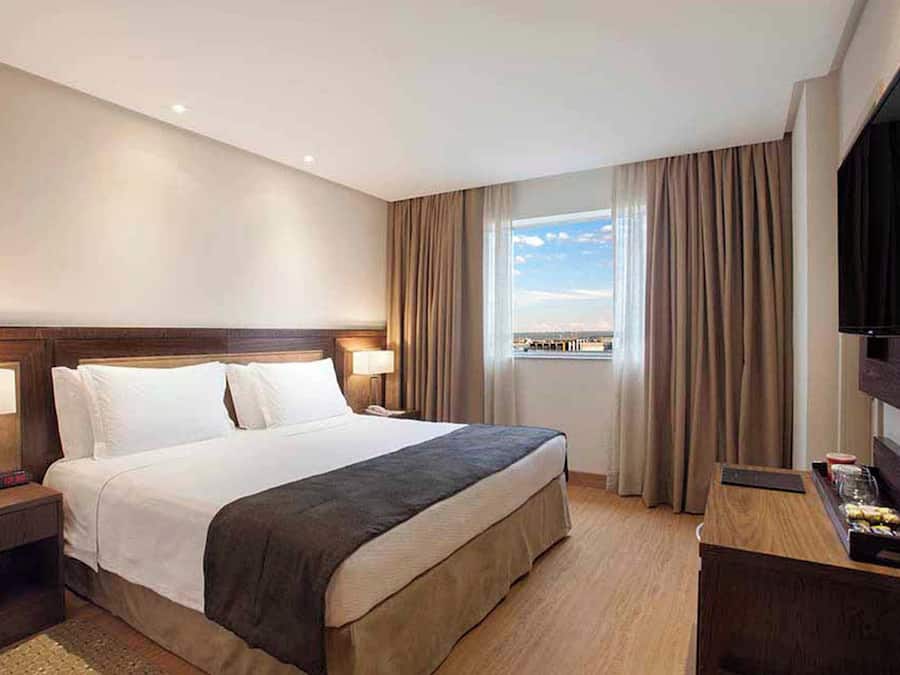 Une chambre d’hôtel avec un lit, des tables de chevet, une télévision et une fenêtre avec des rideaux.