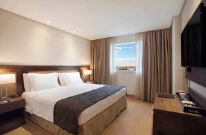 Une chambre d’hôtel avec un lit, des tables de chevet, une télévision et une fenêtre avec des rideaux.