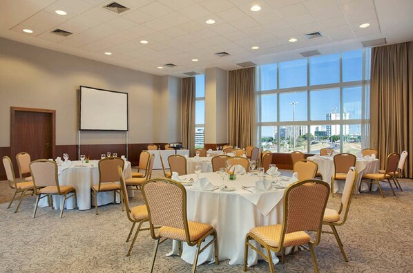 A conference room with round tables, chairs, and a projector screen. - Windsor Brasilia Hotel (Brasília)