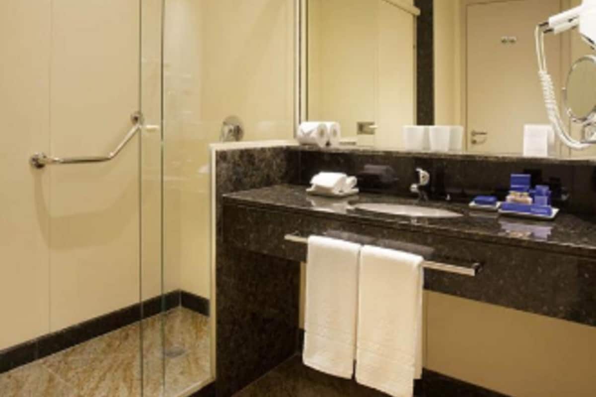Un baño moderno con cabina de ducha de vidrio, suelo de baldosas de mármol, tocador con espejo y secador de pelo.