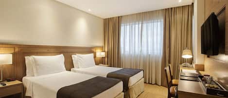 A hotel room with two beds, a desk, a chair, a TV, and a window with curtains.