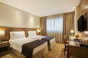 Ein Hotelzimmer mit zwei Betten, einem Schreibtisch, einem Stuhl, einem Fernseher und einem Fenster mit Vorhängen.