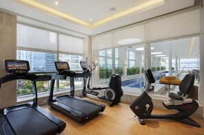 Ein modernes Fitnessstudio mit Laufbändern, einem Ellipsentrainer und einem Rudergerät, großen Fenstern und Blick auf die Stadt.