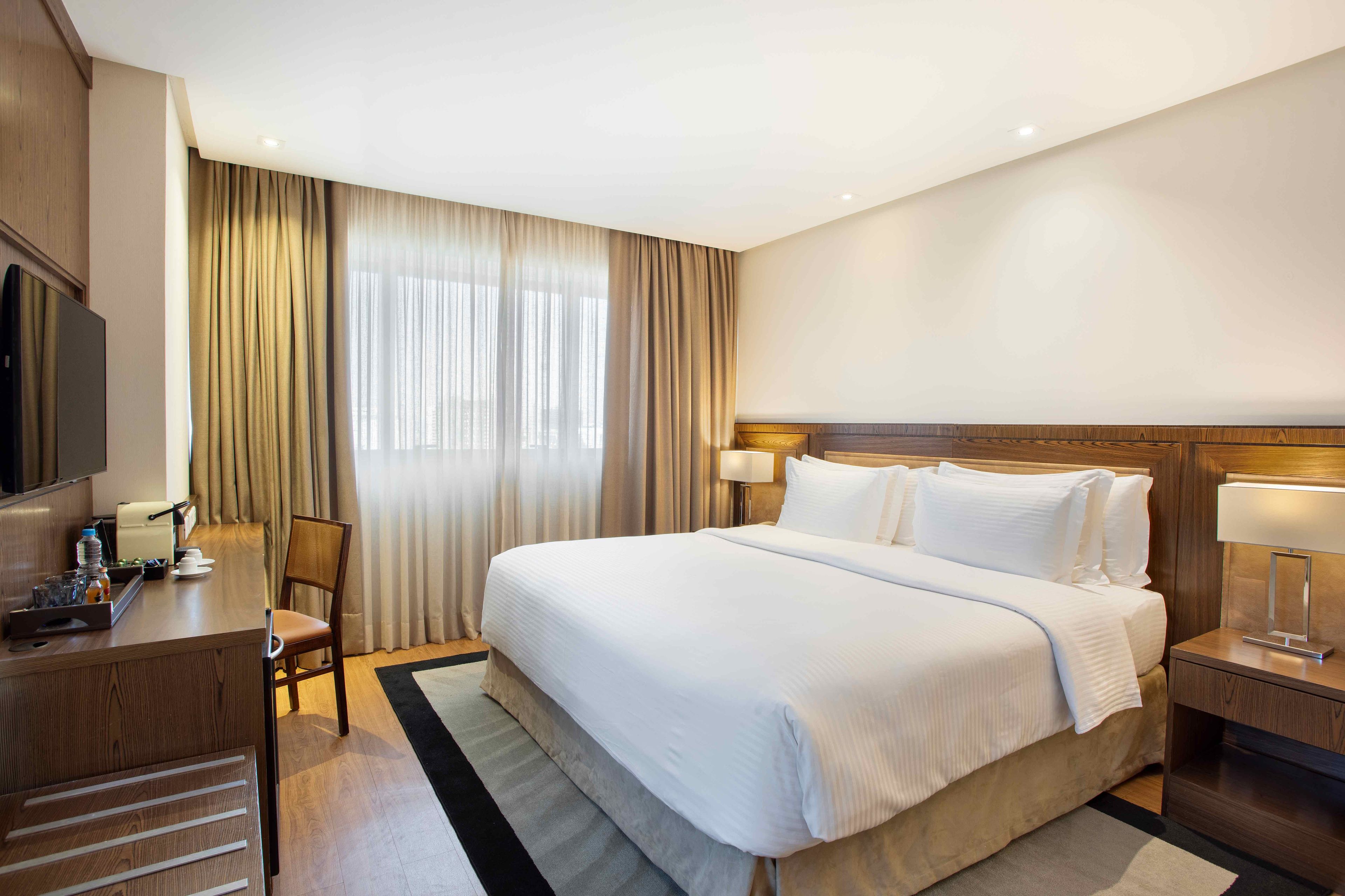 A hotel room with a large bed, a desk with a chair, a television, and a window with curtains.