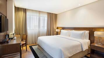 A hotel room with a large bed, a desk with a chair, a television, and a window with curtains.