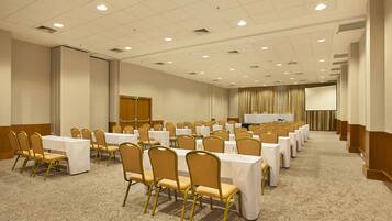 A conference room with rows of tables and chairs, a projector screen, and a stage area.