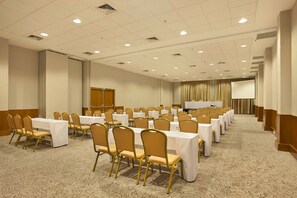 Une salle de conférence avec des rangées de tables et de chaises, un écran de projection et une estrade.