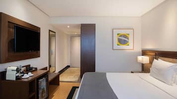 A hotel room with a bed, a TV, a coffee machine, a minibar, and a framed picture on the wall.